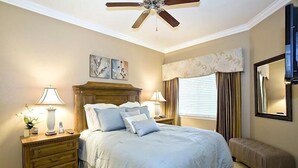 A bedroom with a bed, two bedside tables, a ceiling fan, a window with curtains, and a mirror on the wall. - Reunion Resort - 3 BR Condo, Ground Floor, Patio - JHH 45890 (Kissimmee)
