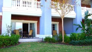 A two-story building with a brick facade, a balcony with white railings, and a small tree in the foreground. - Reunion Resort - 3 BR Condo, Ground Floor, Patio - JHH 45890 (Kissimmee)