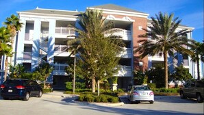 A multi-story building with balconies, parked cars, and palm trees. - Reunion Resort - 3 BR Condo, Ground Floor, Patio - JHH 45890 (Kissimmee)
