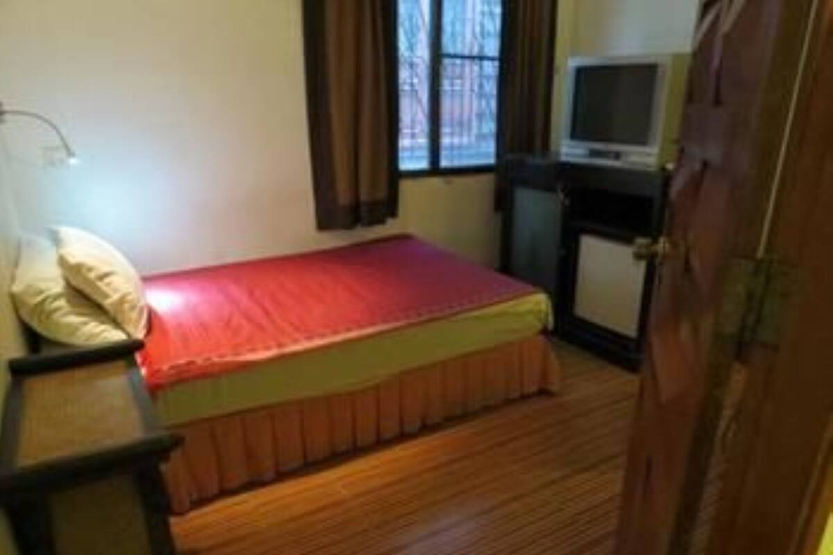 A small bedroom with a single bed, a bedside table, a lamp, a television, and a window with curtains.