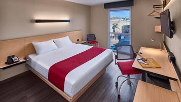 A hotel room with a bed, a desk, a chair, a TV, a phone, and a window with a view of the outside.
