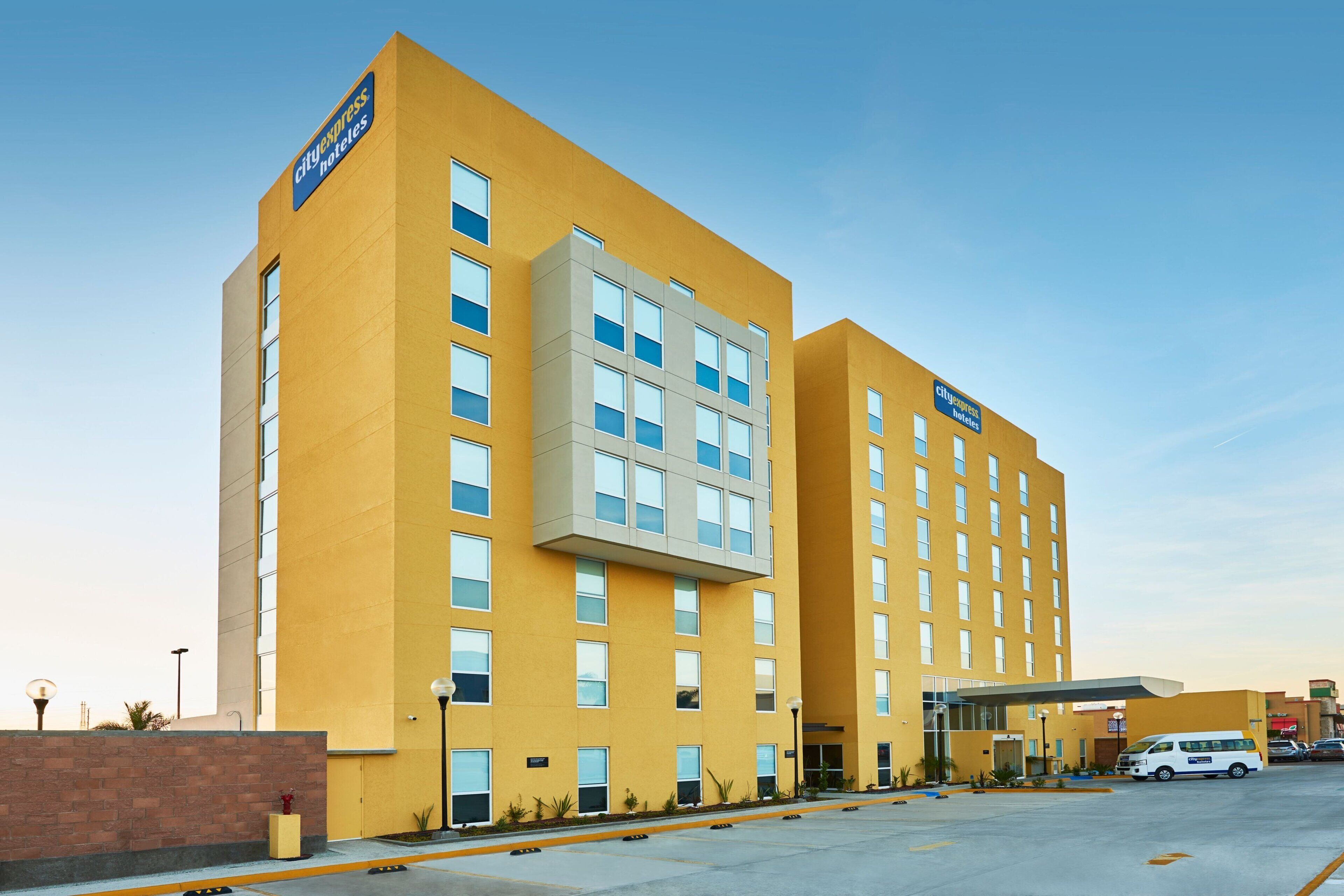 A CityExpress hotel with a modern yellow facade, multiple floors, and a parking area with a white van.