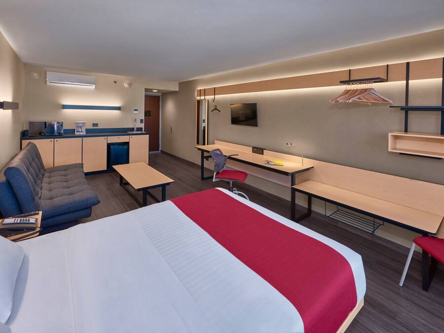 A hotel room with a bed, a desk, a chair, a sofa, and a kitchenette.