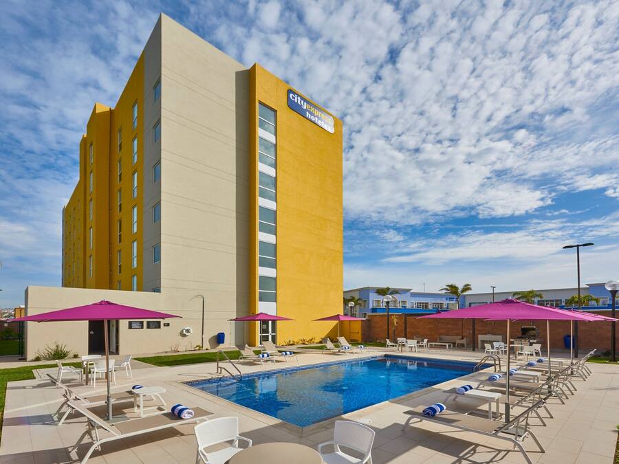 A hotel with a pool area, including lounge chairs and umbrellas.