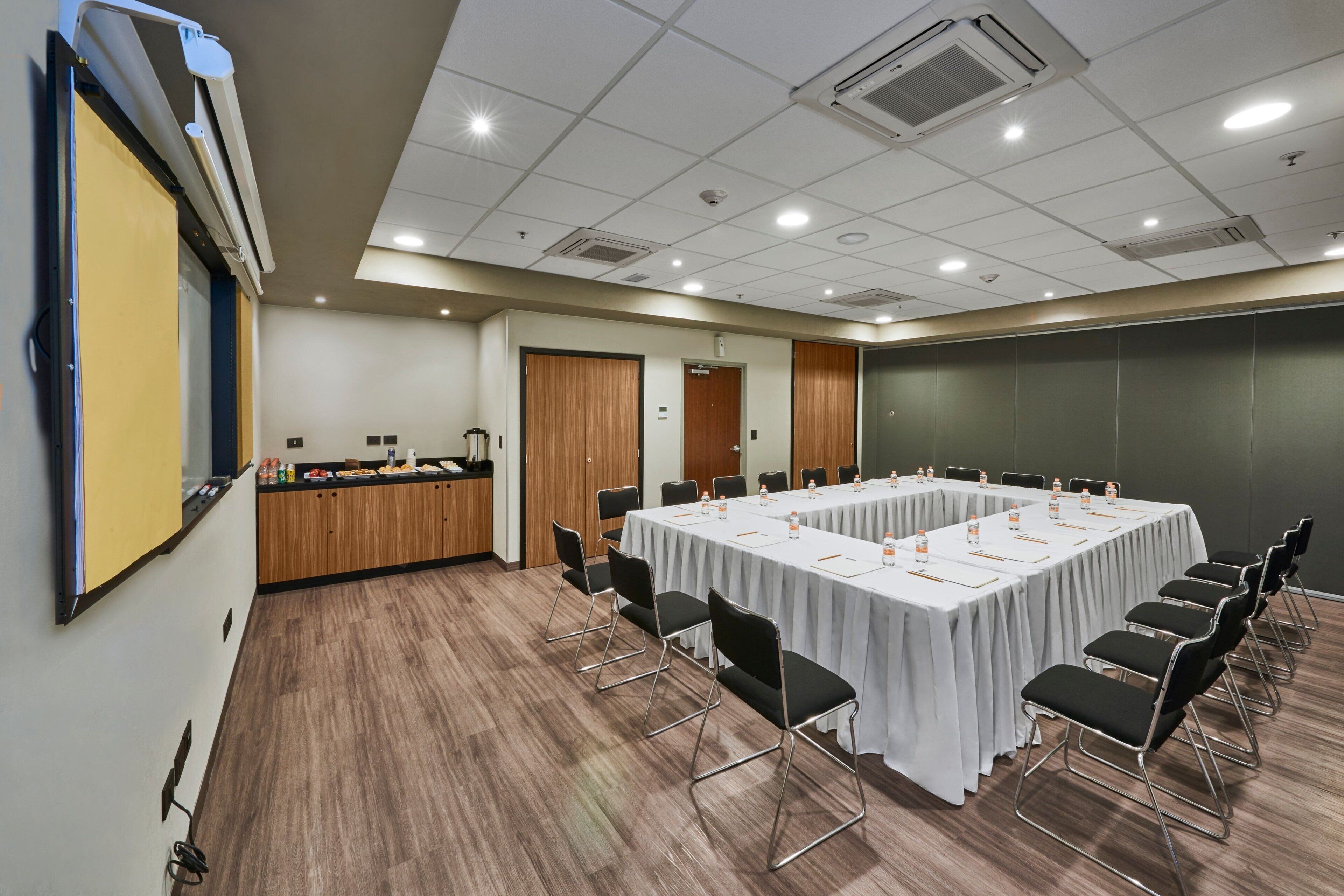 A conference room with a long table, black chairs, and a projector screen.