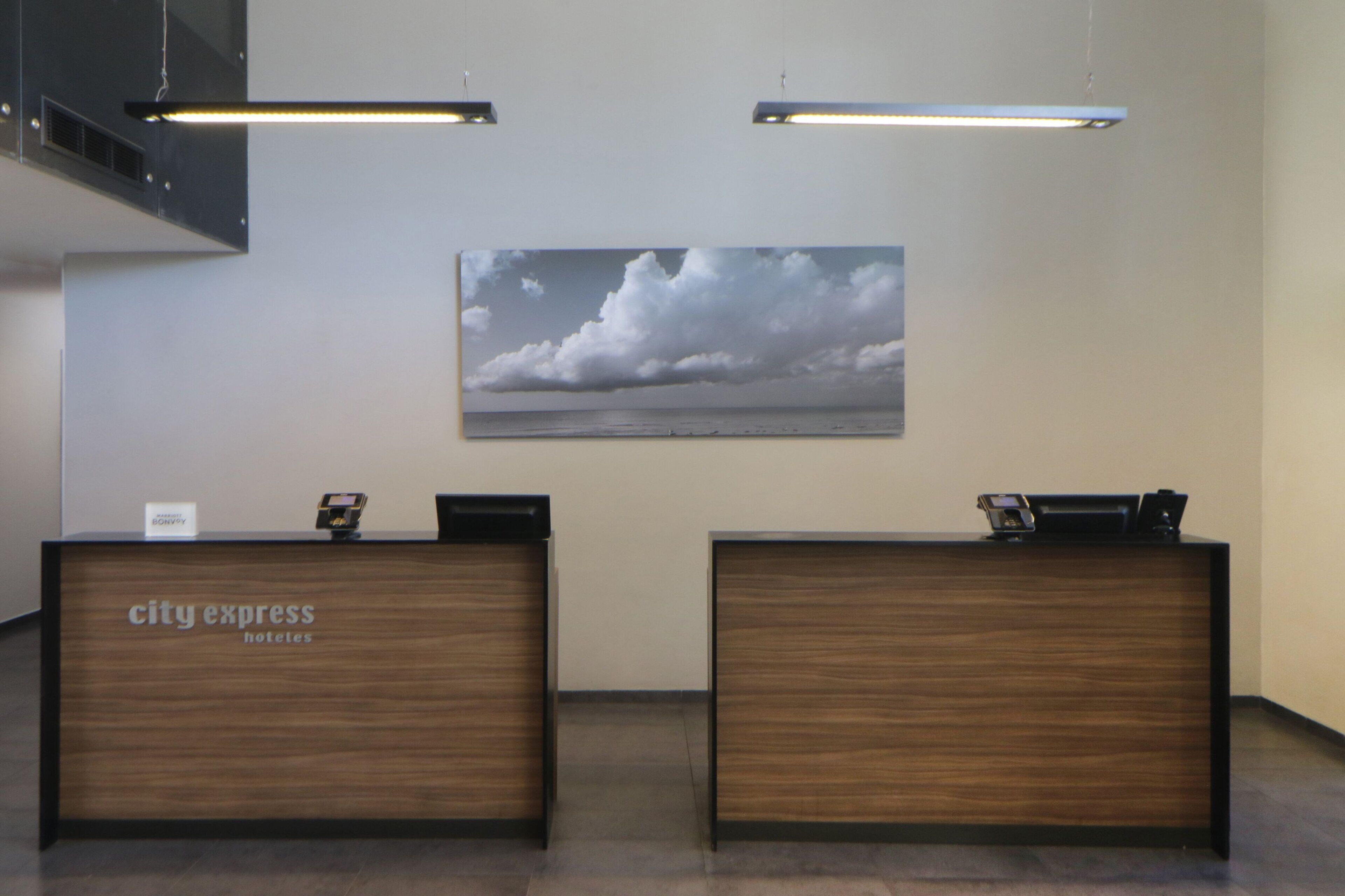 A reception desk with a 'City Express Hotels' sign, two receptionists' stations, and a large cloud painting on the wall.