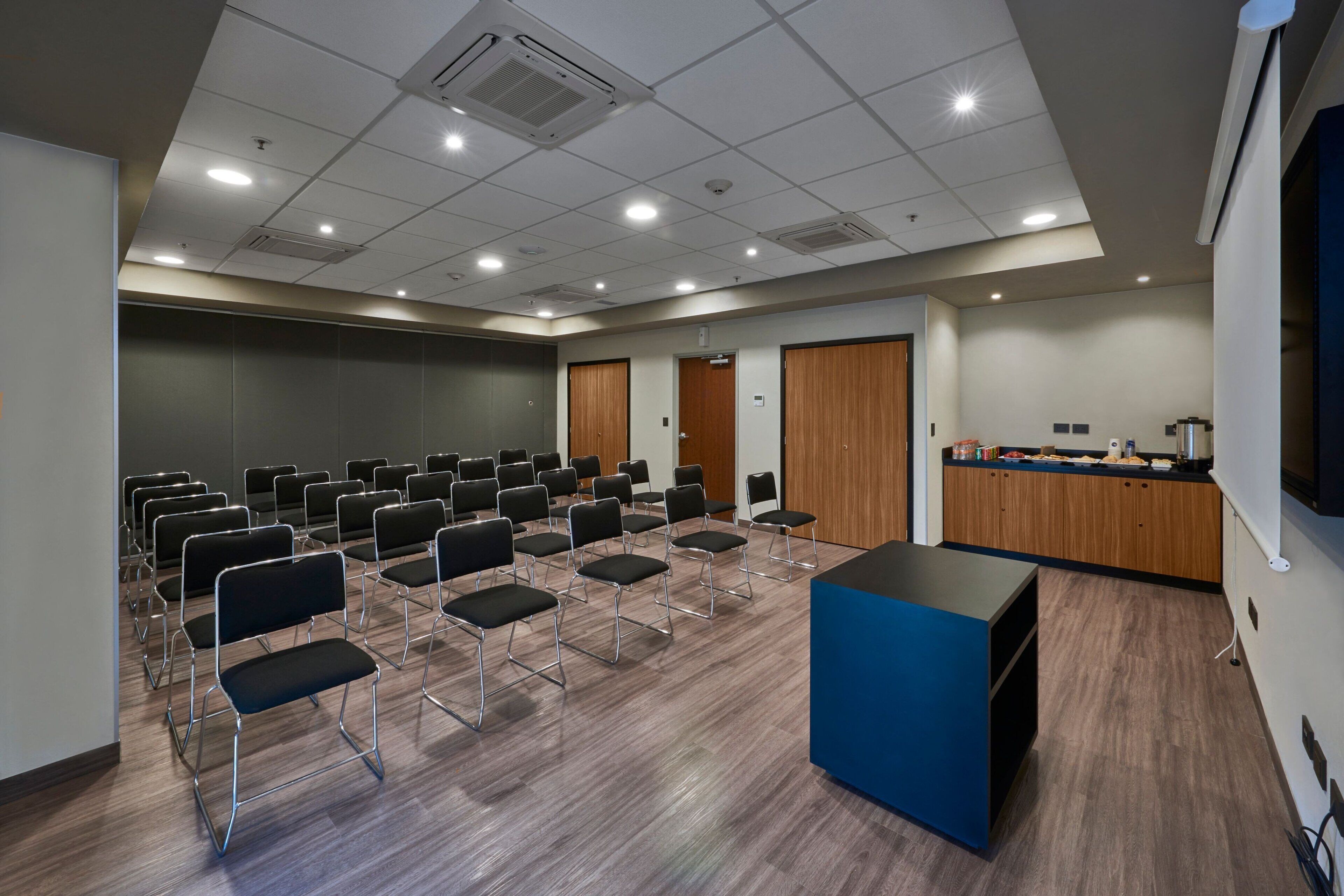 A conference room with rows of chairs, a podium, and a kitchenette area.