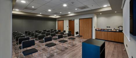 A conference room with rows of chairs, a podium, and a kitchenette area.