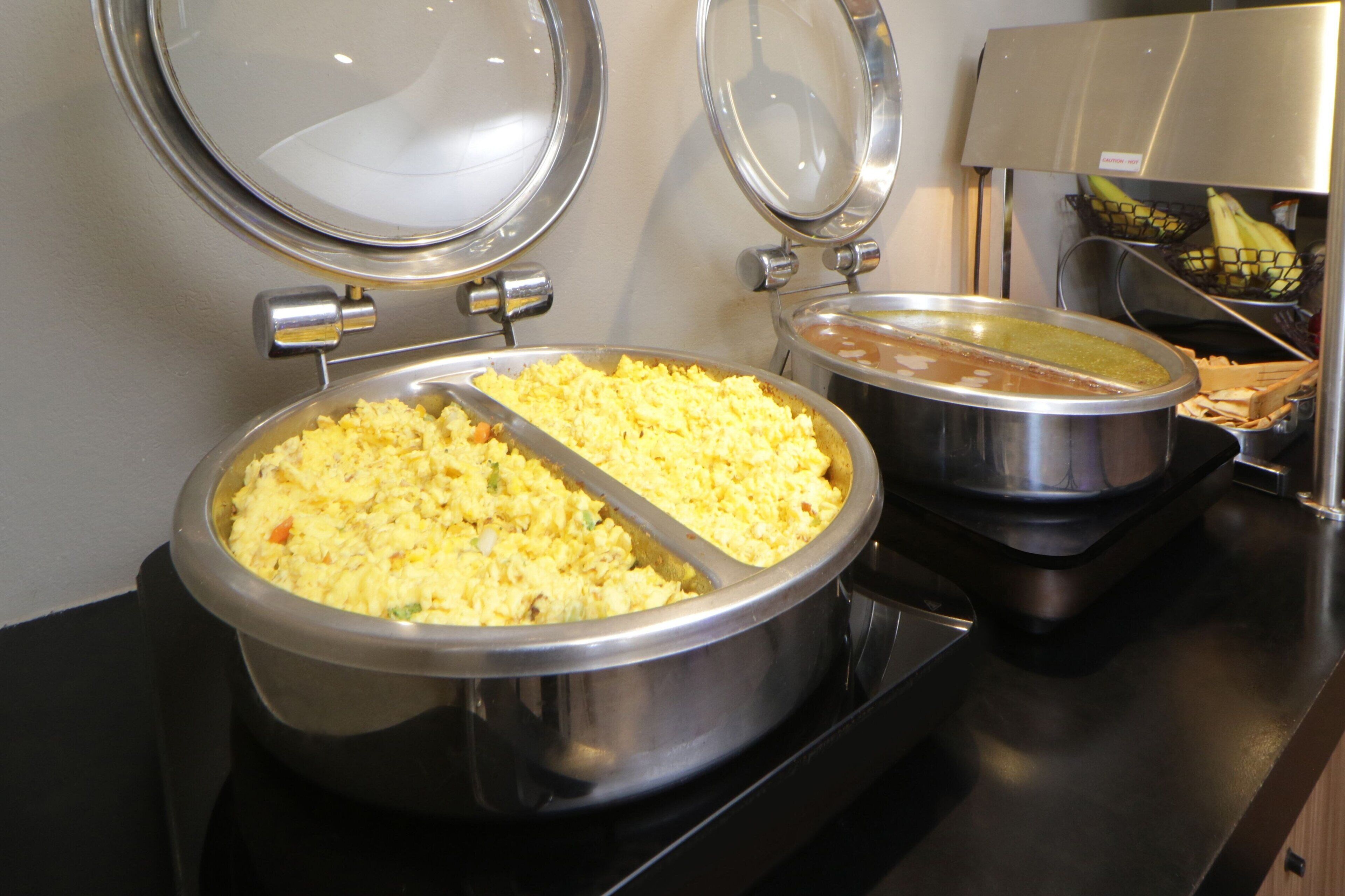 A buffet setup with two large metal serving dishes, one containing scrambled eggs and the other a brown sauce.