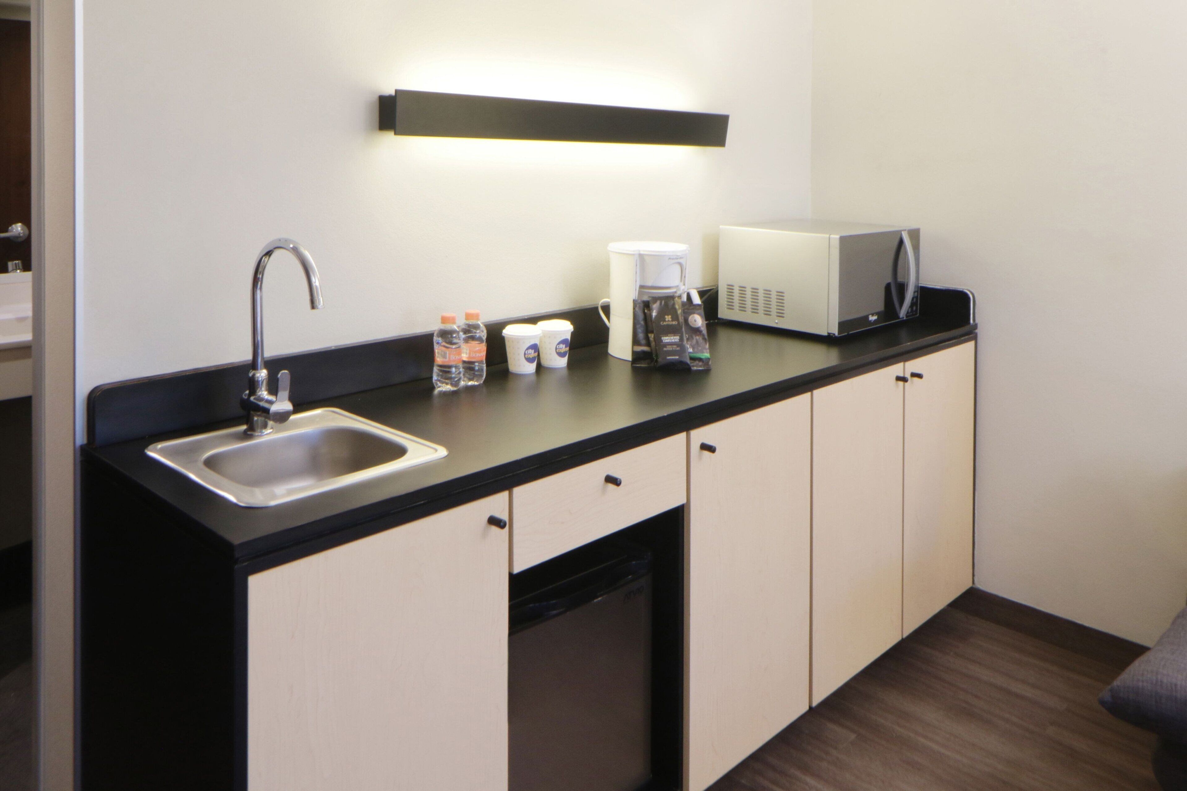 A modern kitchenette with a sink, coffee maker, microwave, and cabinets.