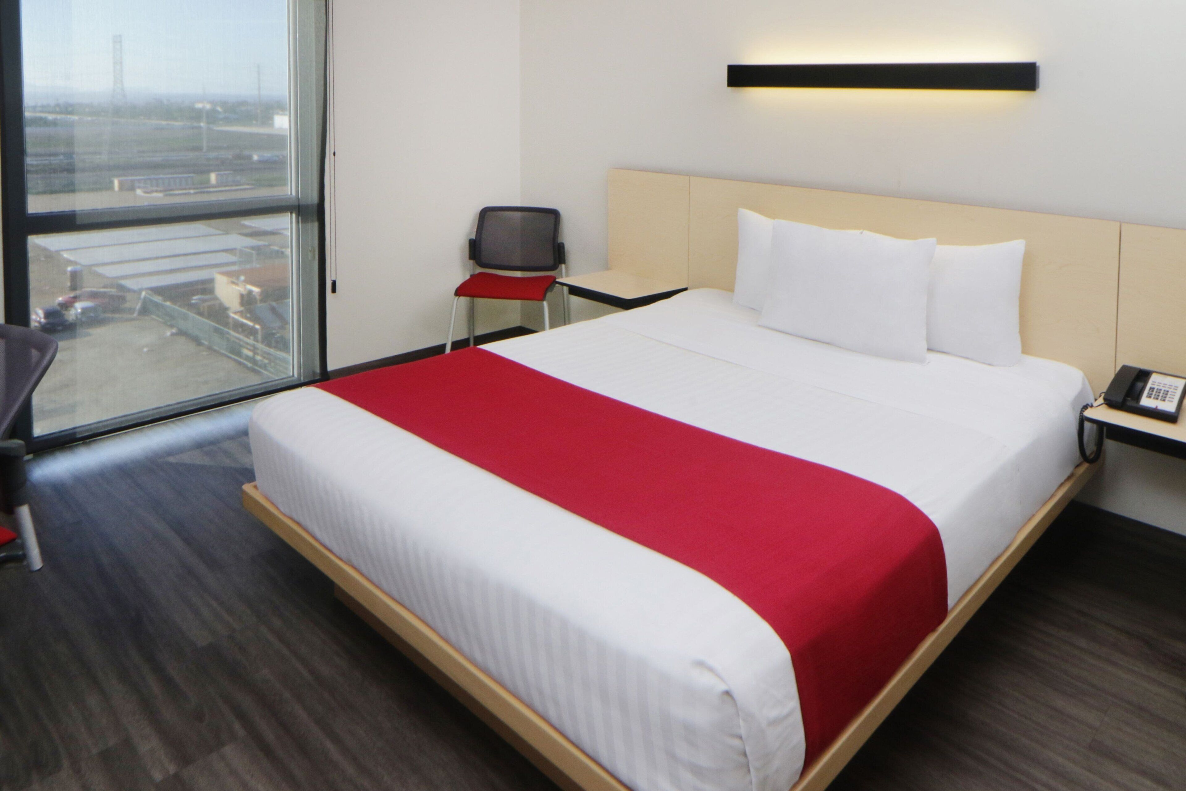 Habitación de hotel con una cama grande, un escritorio, una silla y vista al aeropuerto.