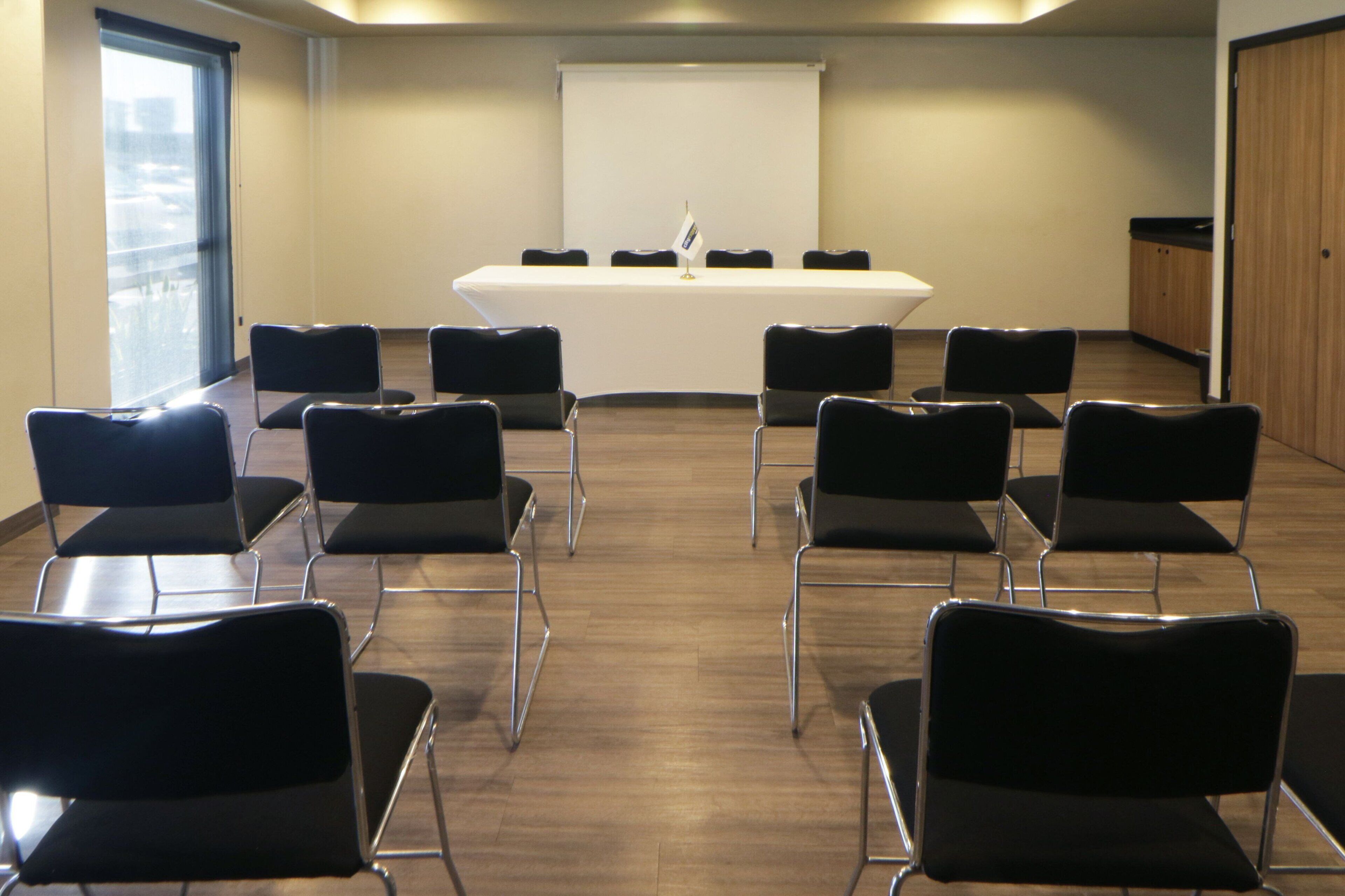 Una sala de conferencias con una mesa larga, ocho sillas y una pantalla de proyector.