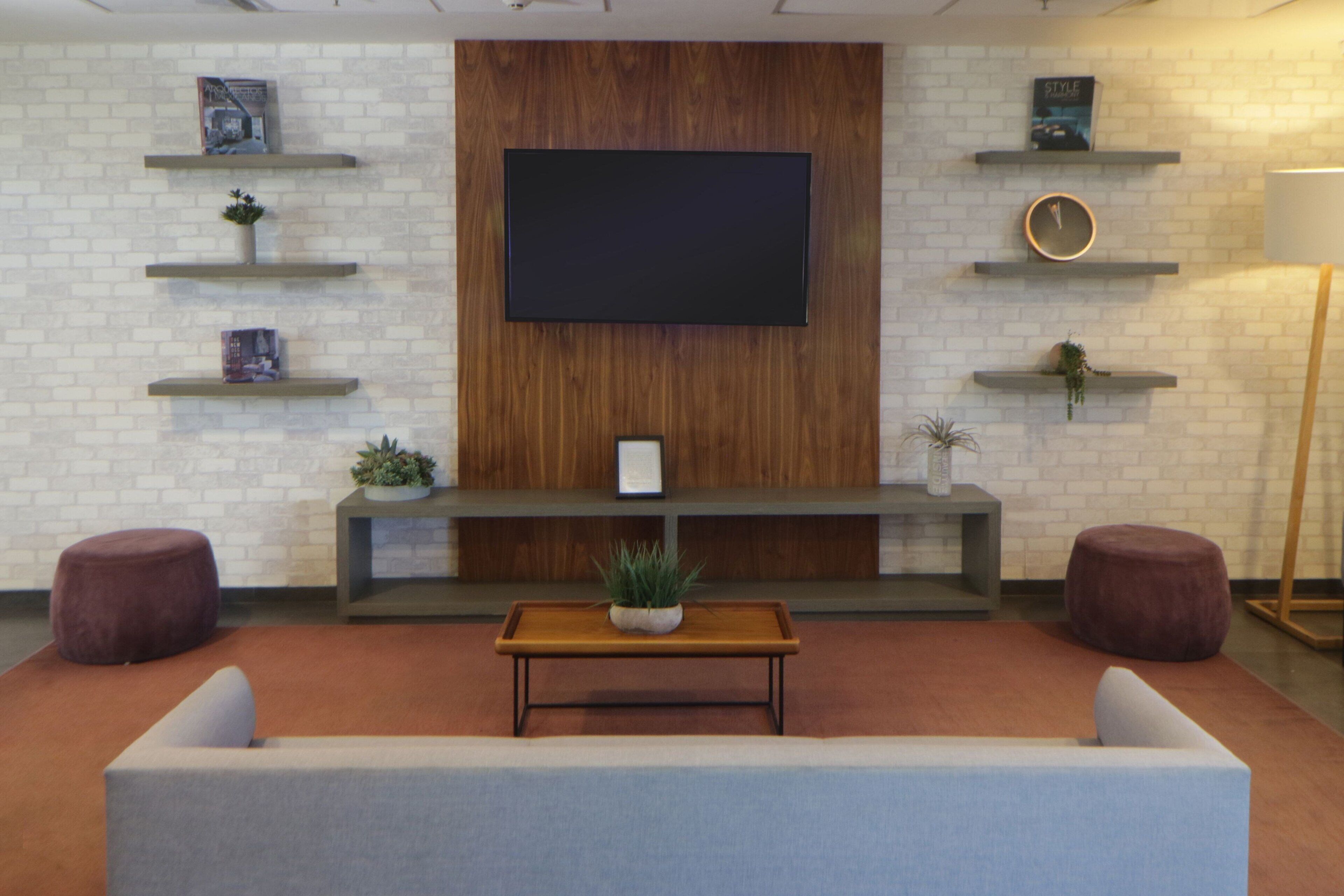 A modern living room with a flat-screen TV mounted on a brick wall, a wooden bench, and two round ottomans.