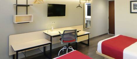 A hotel room with a desk, chair, two beds, a TV, a mirror, and a wardrobe.