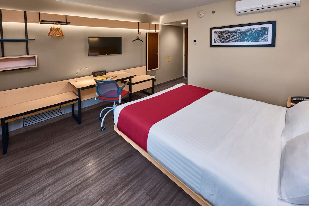 A hotel room with a bed, a desk, a chair, a TV, and a wardrobe.