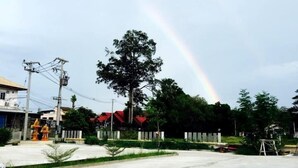 A parking lot with a large tree and a rainbow in the background. - Won DD Place (Roi Et)