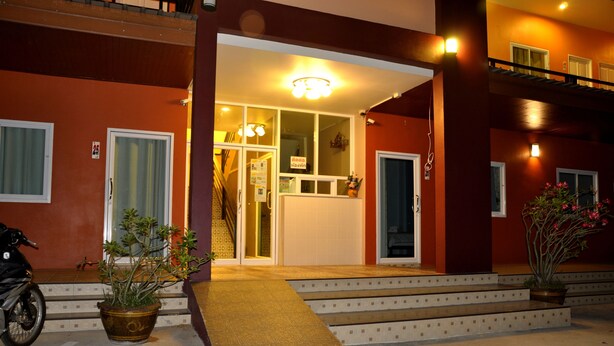 A hotel entrance with a staircase leading to the main door, a potted plant on the left, and a motorcycle parked outside. - Won DD Place (Roi Et)