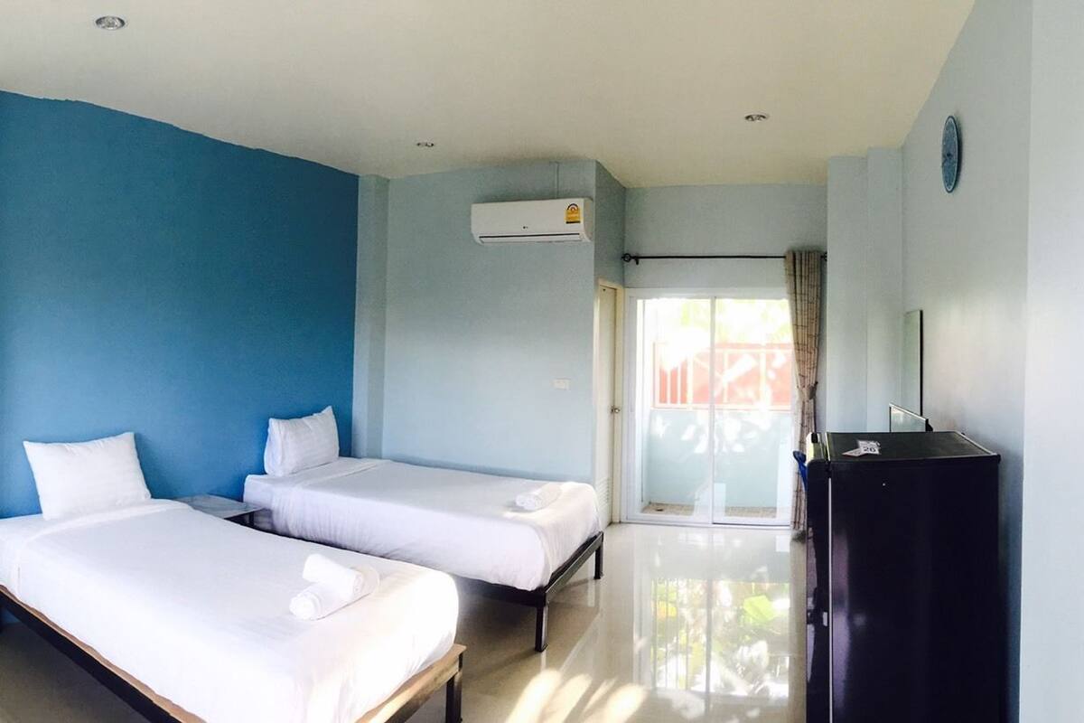 Habitación de hotel con dos camas individuales, un armario negro y un gran ventanal corredero que da a un balcón.