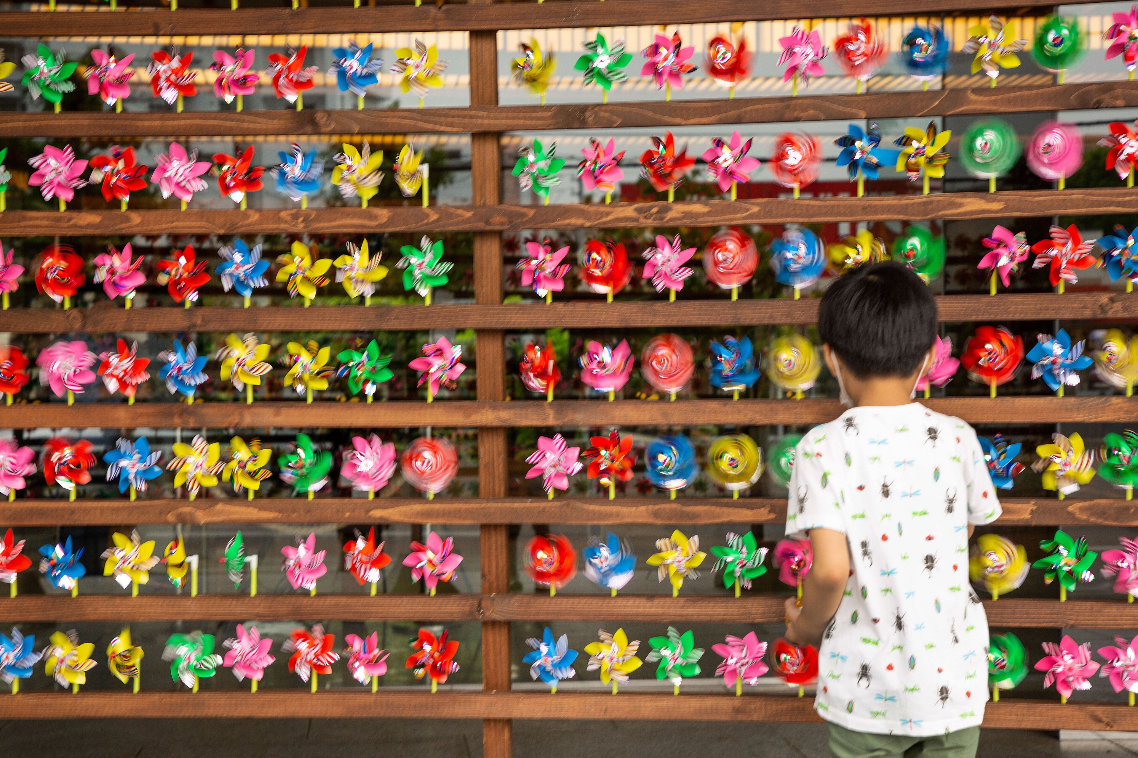 A child standing in front of a wall with multiple rows of colorful pinwheels.