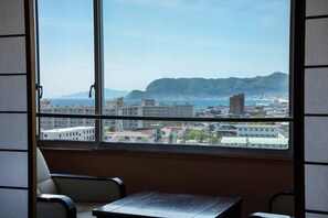 A room with a large window offering a view of a coastal cityscape, including buildings and a hill. - Yumoto Takubokutei (Hakodate)