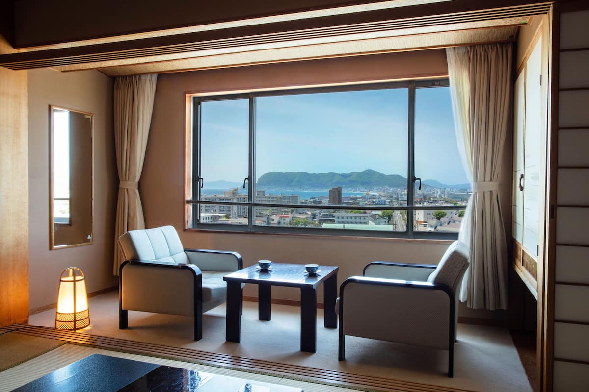 Une pièce avec une grande fenêtre, un canapé, une petite table et un lampadaire.