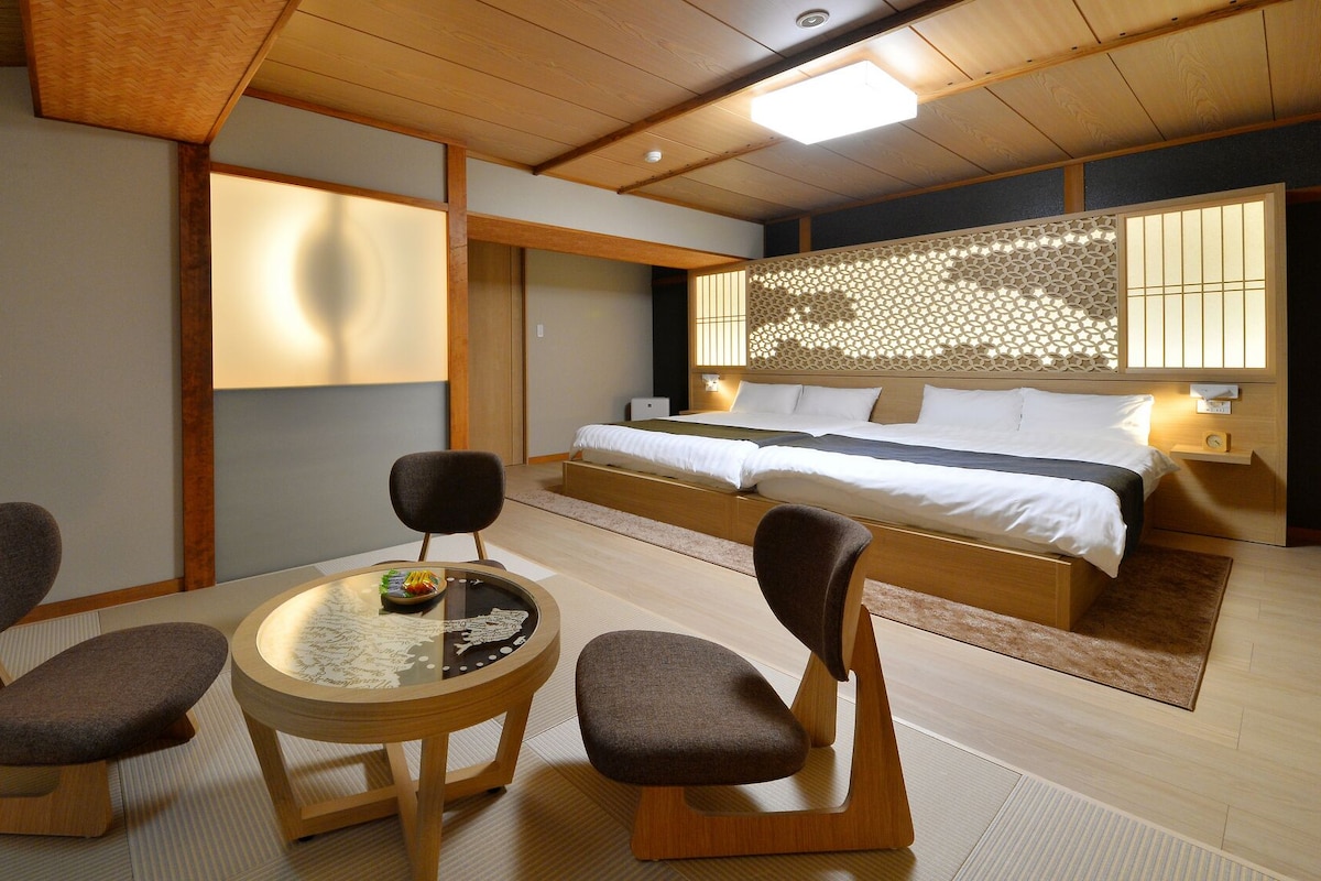 A hotel room with a bed, two chairs, a small table, and a decorative wall.