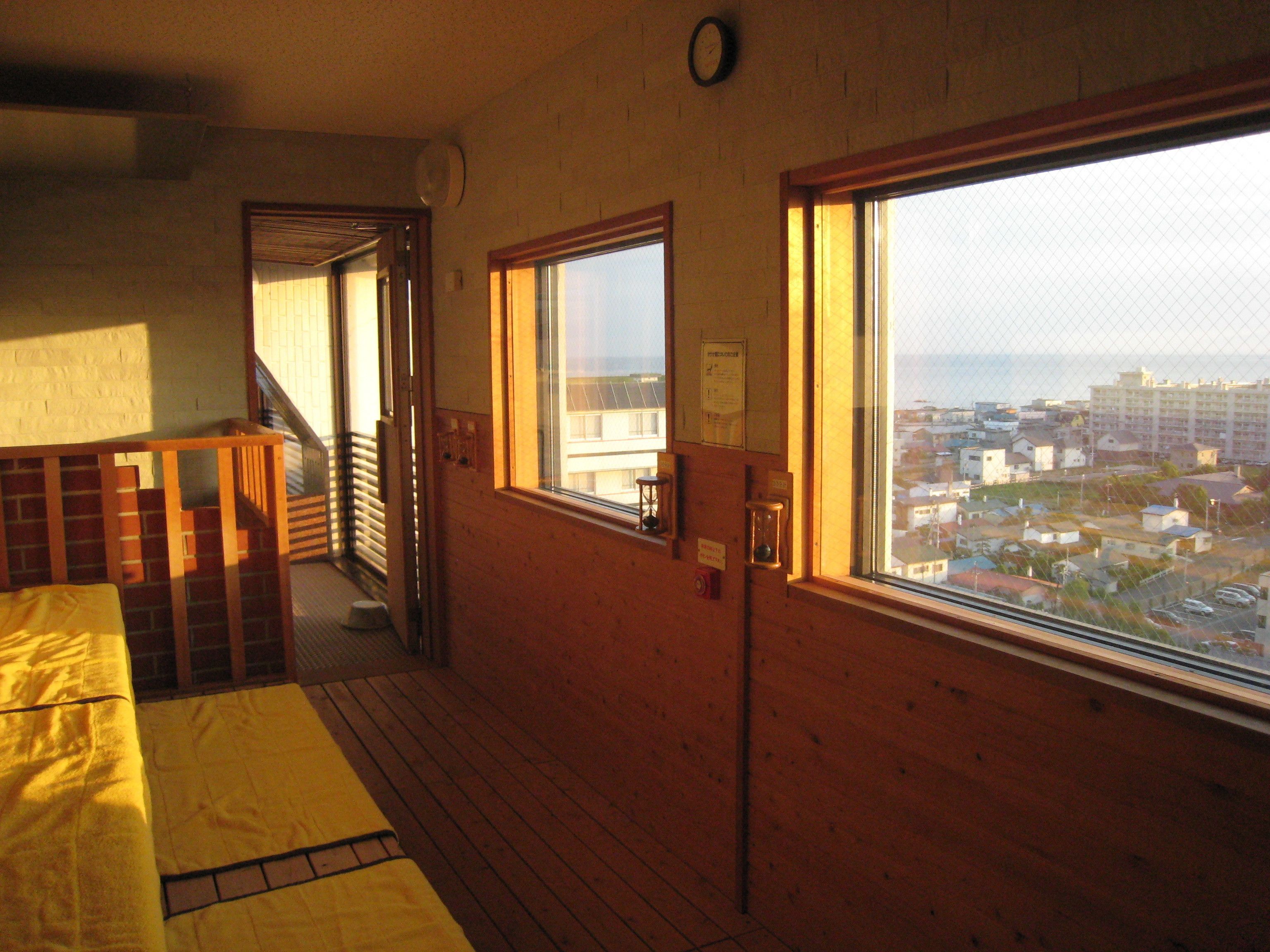A room with wooden walls, a window with a view of a cityscape, a wooden staircase, and a bed with a yellow blanket.