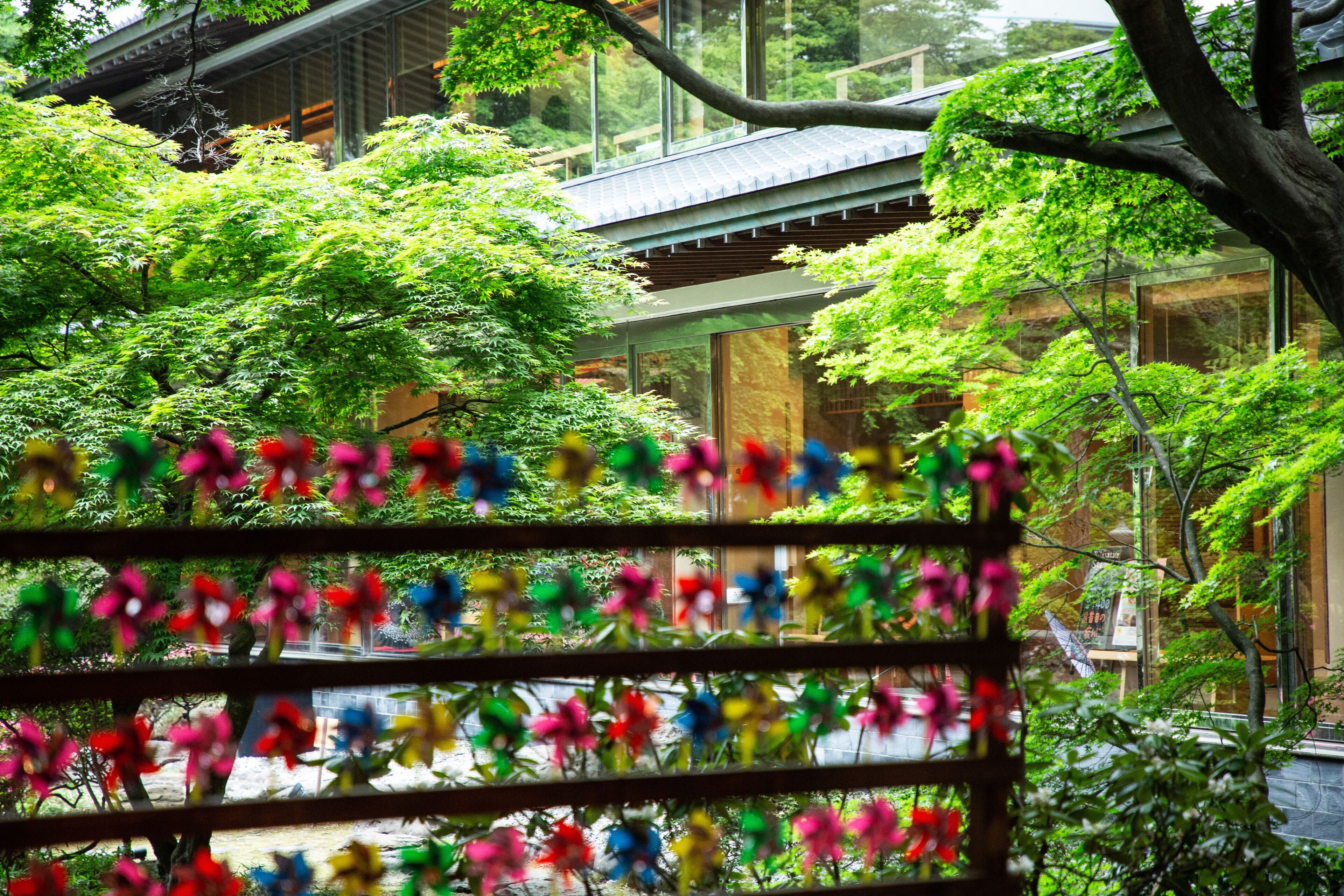 A traditional Japanese building with a modern glass extension, surrounded by lush greenery and a colorful flower display.