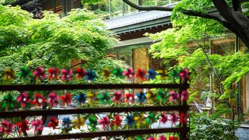 A traditional Japanese building with a modern glass extension, surrounded by lush greenery and a colorful flower display.