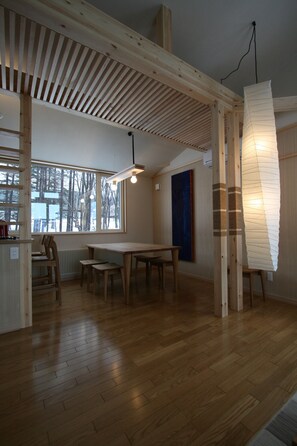 Una habitación amplia con piso de madera, un ventanal con vistas a árboles, una mesa de comedor y una original lámpara de papel.