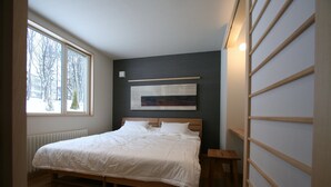 Et soveværelse med en træseng, et stort vindue, en radiator og en vægmonteret hylde.
