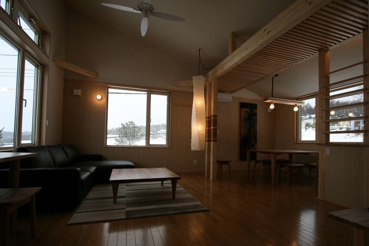 A spacious living room with a wooden floor, a black leather sofa, a coffee table, and a dining area with a table and chairs.