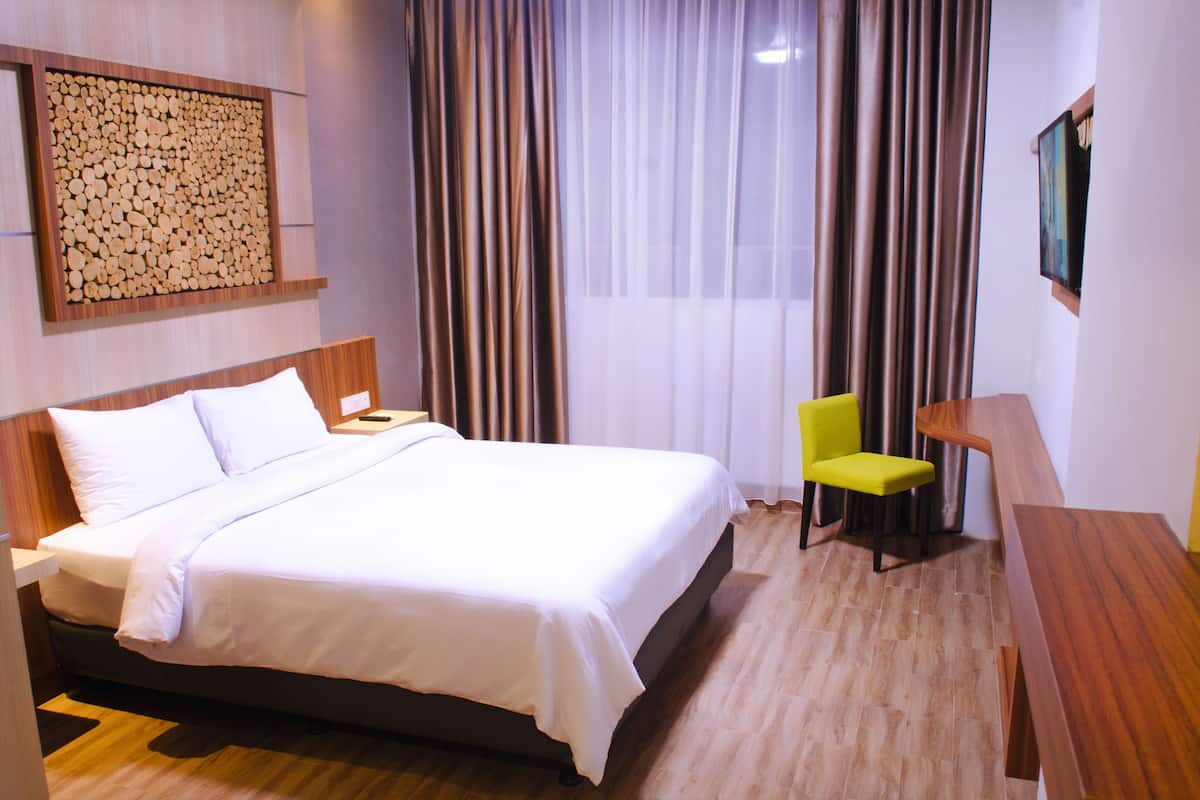 Ein Hotelzimmer mit einem großen Bett, einem Holz-Kopfteil, einem Schreibtisch mit Stuhl und einem Bild an der Wand.