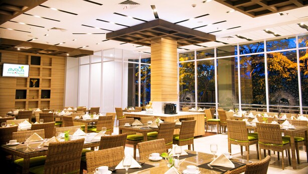 Un comedor amplio con mobiliario de mimbre, una barra central y ventanas grandes que dan a vistas de árboles.
