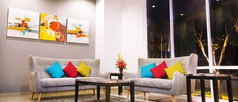 A modern living room with two sofas, colorful cushions, a coffee table, and abstract art on the wall.