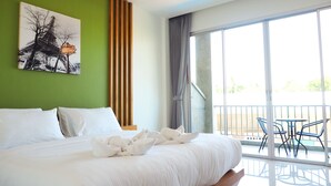 Una habitación de hotel con una cama grande, una pared verde, un cuadro de la Torre Eiffel y un balcón con sillas.