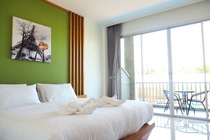 Quarto de hotel com uma cama grande, parede verde, pintura da Torre Eiffel e varanda com cadeiras.