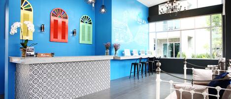 Zona de recepción con una pared azul, un mostrador estampado y una cama blanca con almohadones.