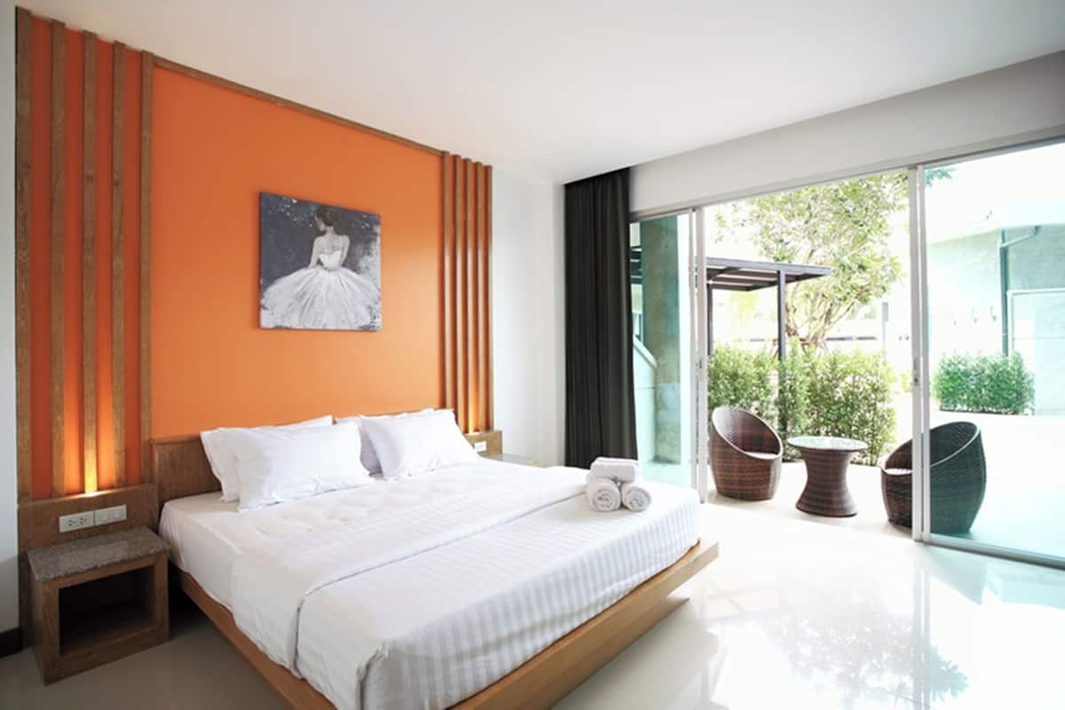A modern hotel room with a large bed, a painting on the wall, and a view of the outdoors through large windows.