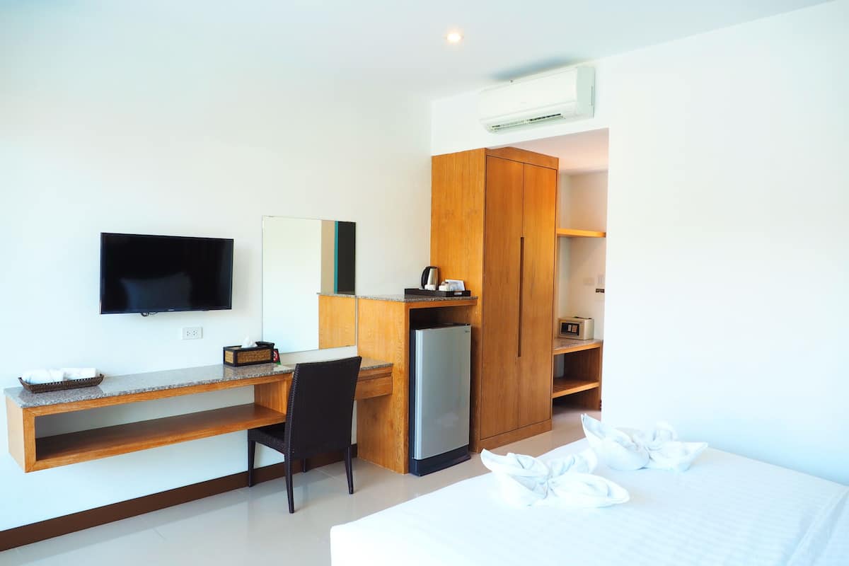 A hotel room with a bed, a desk with a chair, a television, a refrigerator, and a wardrobe.