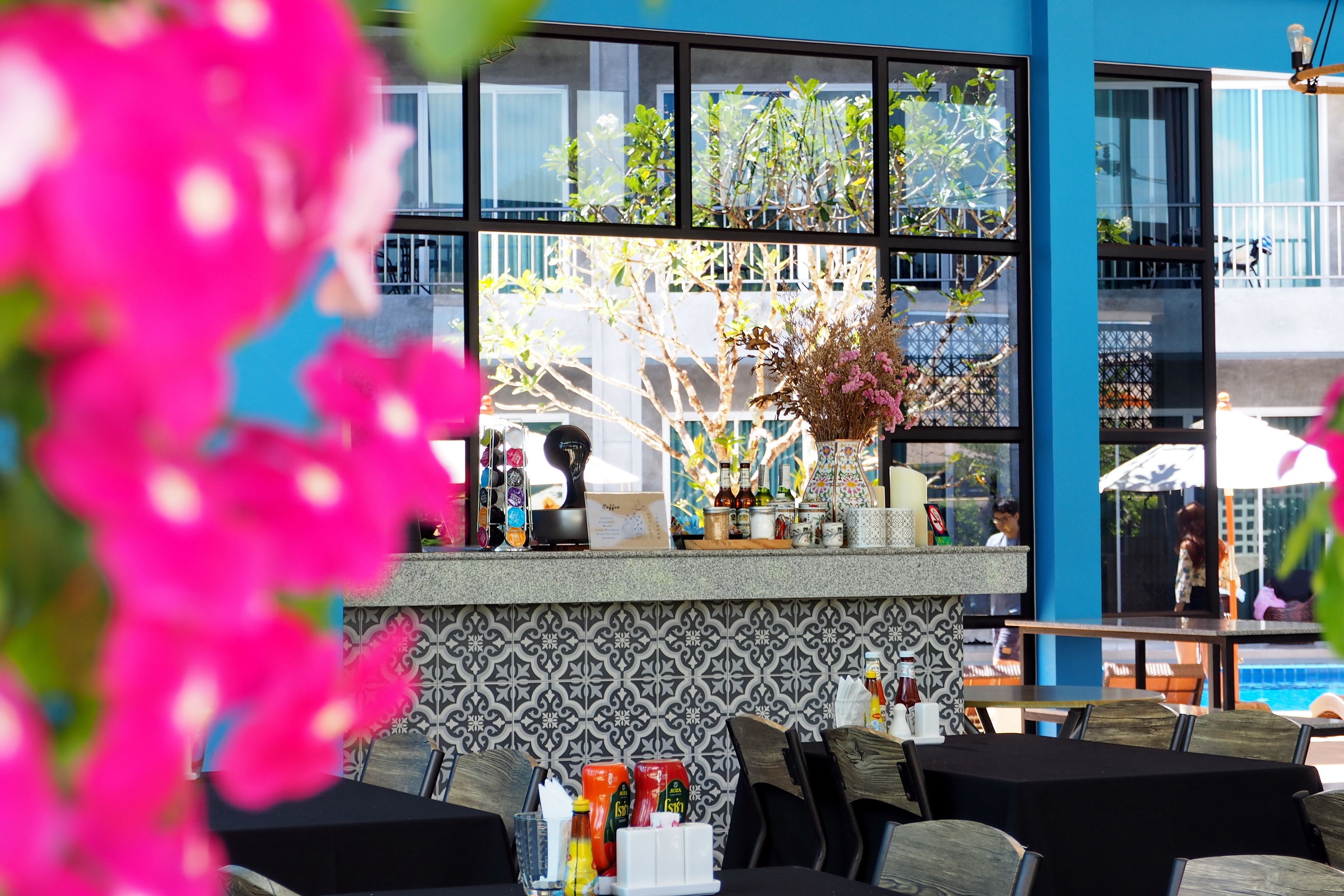 A restaurant with outdoor seating, a bar area with bottles and glasses, and a view of a pool.