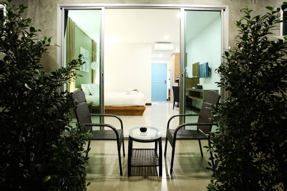 A modern hotel room with a glass door leading to a bedroom, a small table with chairs, and potted plants.