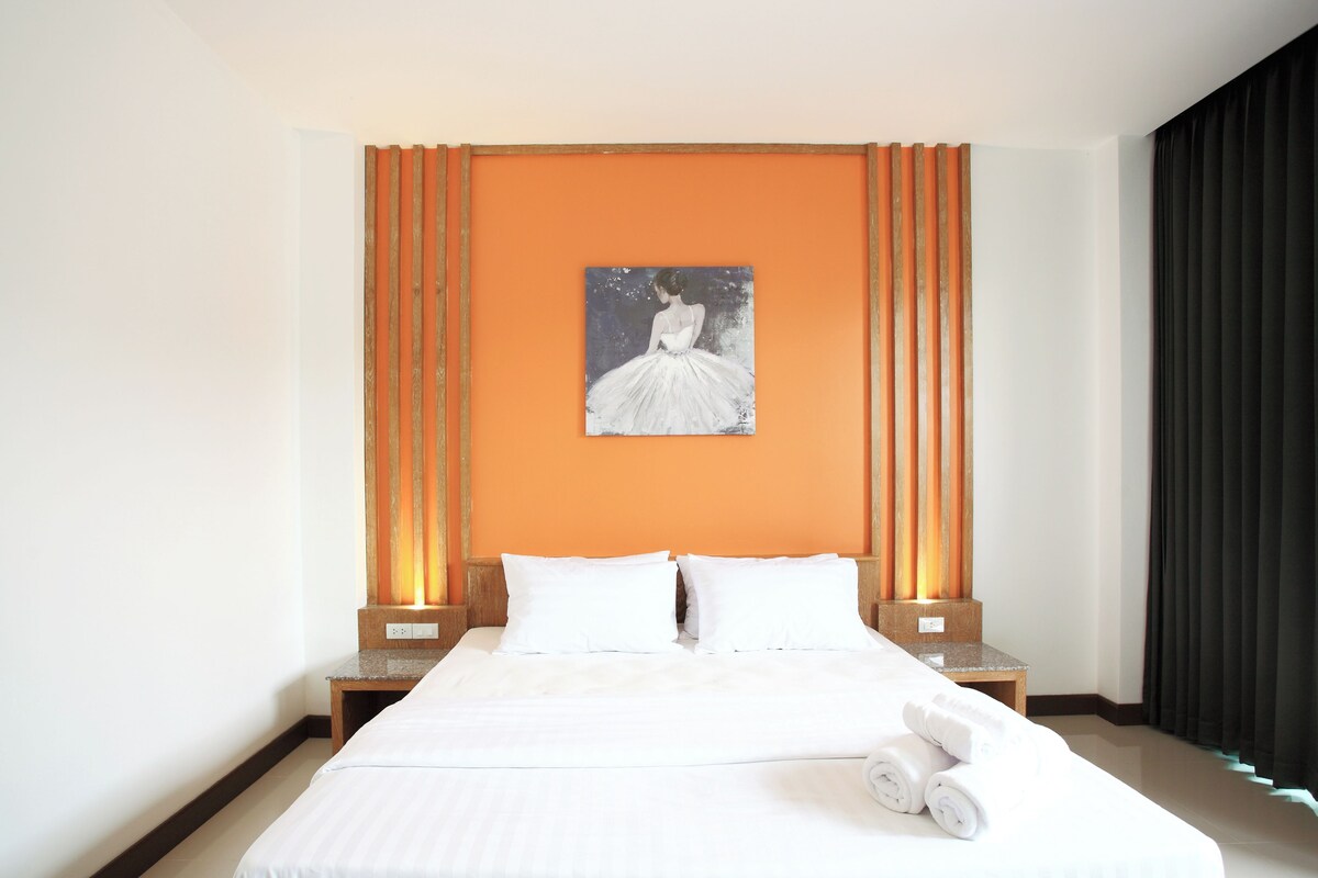 A hotel room with a large bed, two bedside tables, a painting on the wall, and a window with curtains.