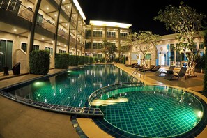 A swimming pool with a tiled edge, surrounded by lounge chairs and a building with multiple balconies. - The Malika (Phuket)