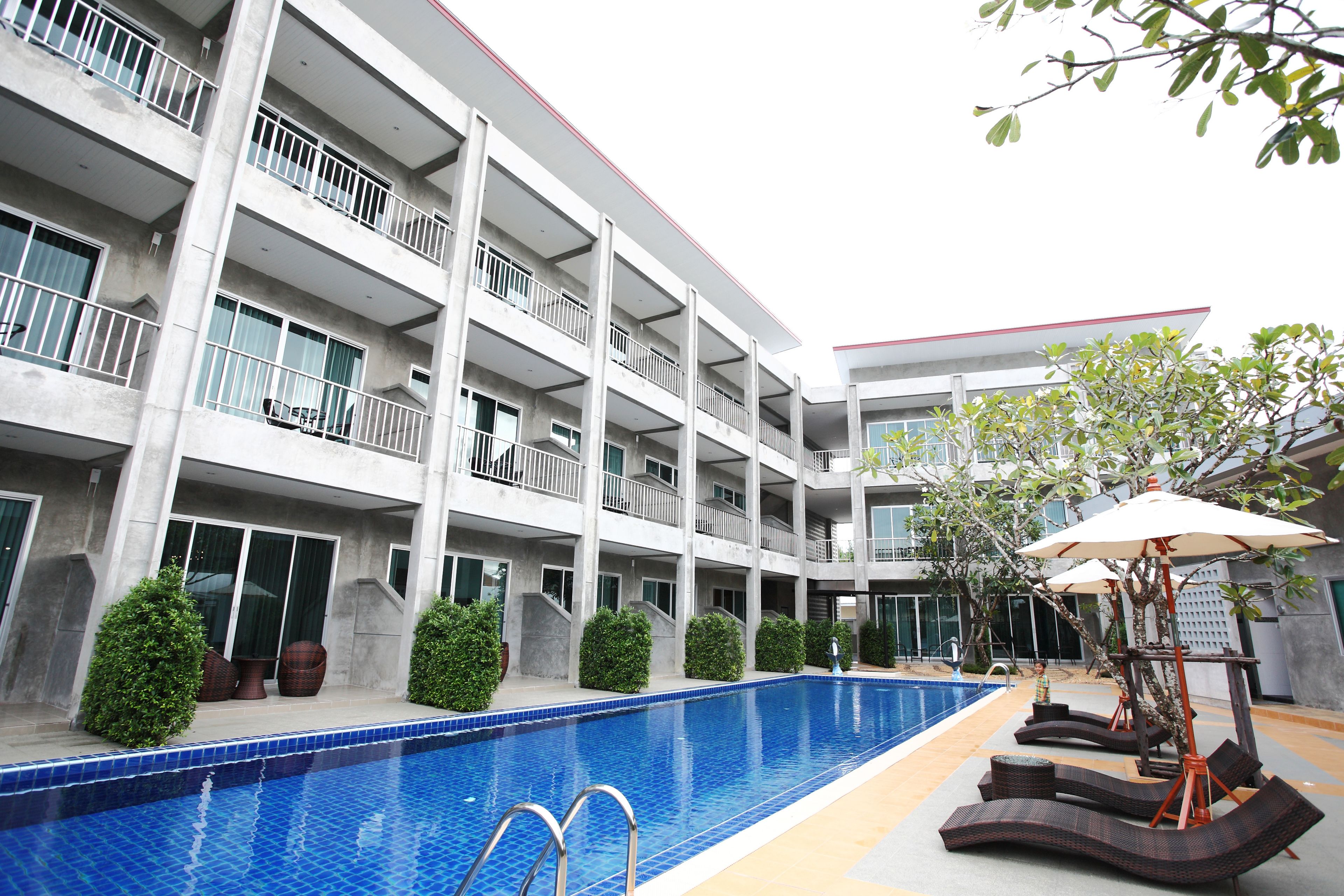 A multi-story hotel with a swimming pool, outdoor seating, and a well-maintained garden.