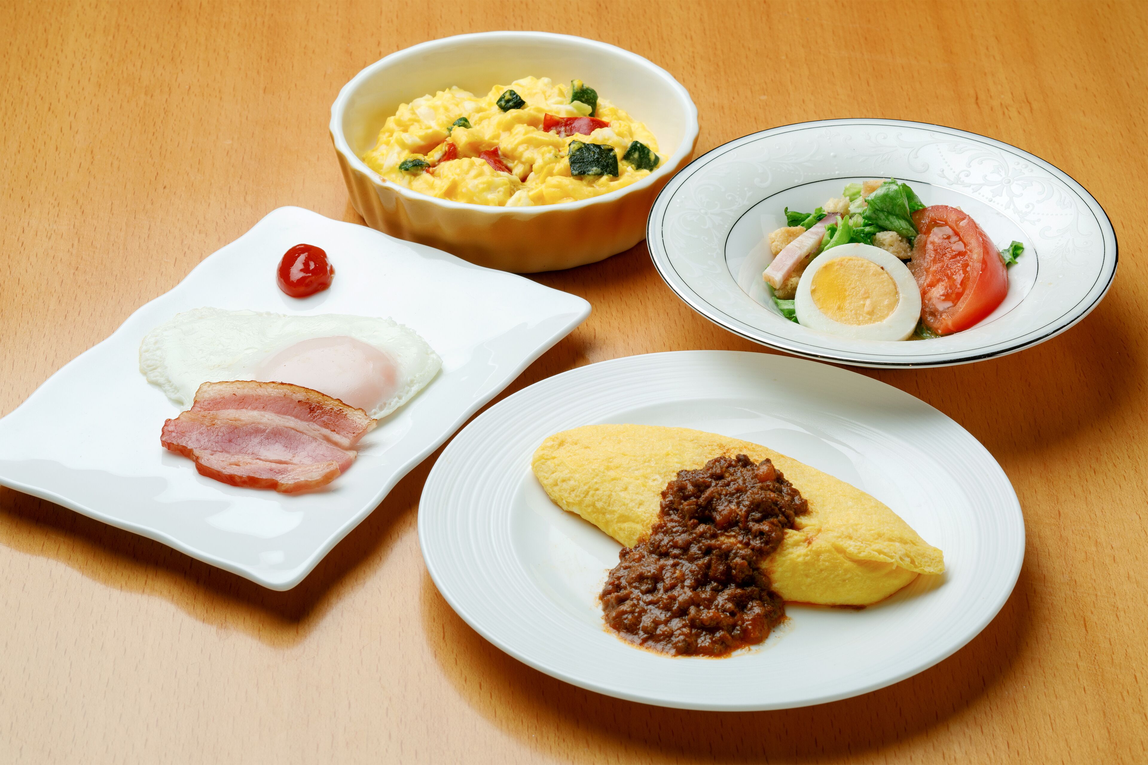 Una mesa con tres platos de comida: huevos revueltos con tocino, una ensalada con huevo duro y una tortilla con carne.