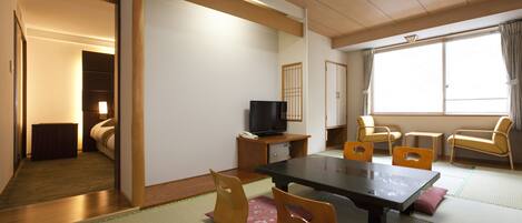 A traditional Japanese room with tatami flooring, a low table with chairs, a television on a cabinet, and a sliding door leading to another room.