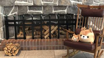 A stone fireplace with a black metal screen, a wooden chair with a plush toy, and a stack of firewood.