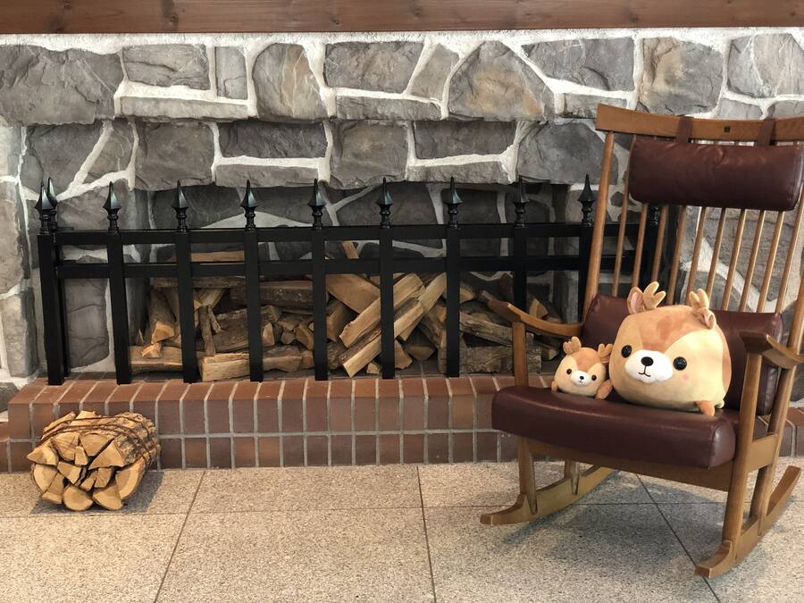 A stone fireplace with a black metal screen, a wooden chair with a plush toy, and a stack of firewood.