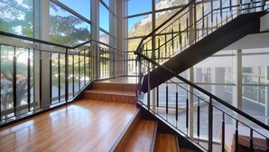 A spacious interior with a wooden floor, a glass railing staircase, and large windows offering a view of a mountainous landscape.